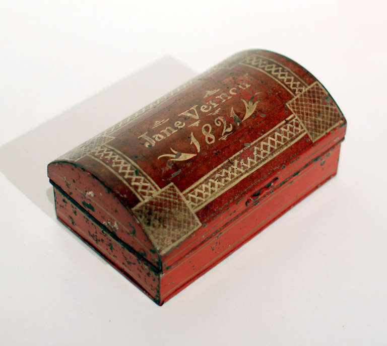 Charming little tole painted dome top work box with red ground and gold painted borders and owner's name, Jane Vernon, and dated 1821. Interior is compartmented and with a pin cushion in one corner. The original sifter, for fine sand or powder, is