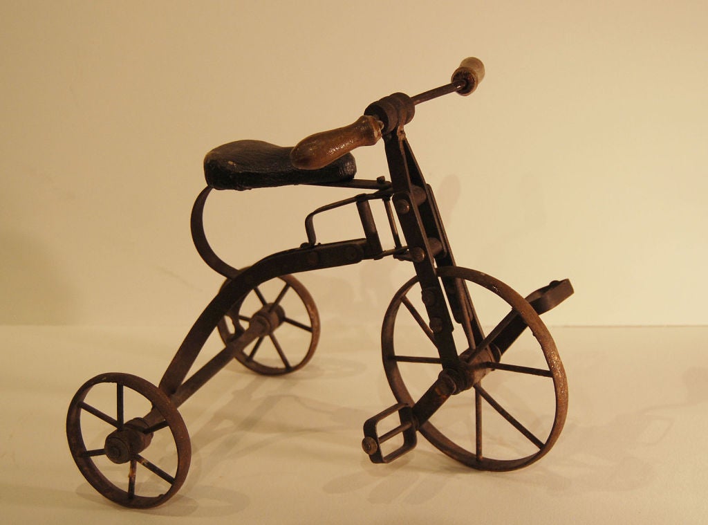 Eccentric miniature iron tricycle with leather seat and wooden handles. Circa 1900.