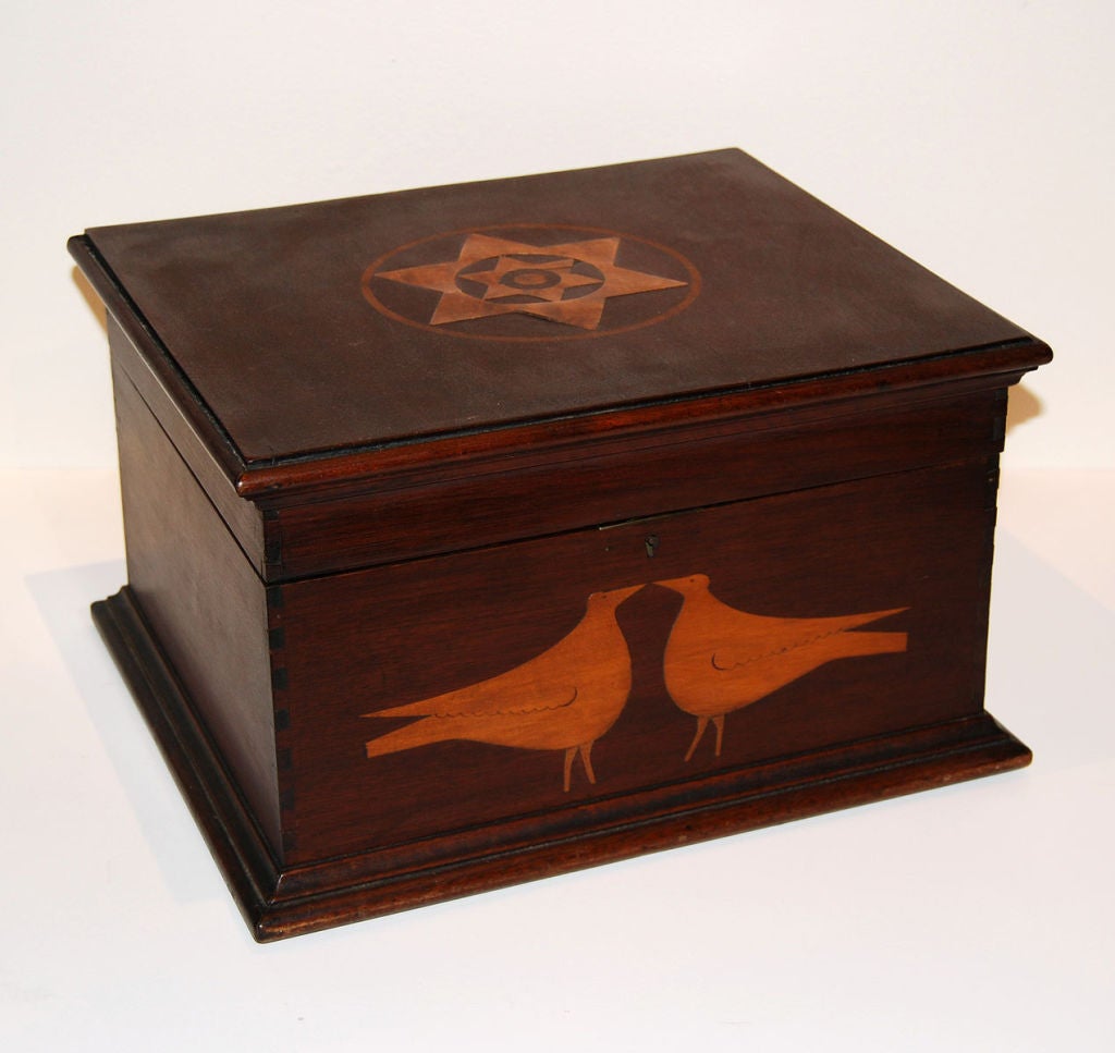 Finely made mahogany box with dovetails and moldings. A pair of outstanding birds is inlaid in maple on the front, and a graphic double star design encircled on the top, also of maple inlay. Inside is a tray with a handle, which sits at the top of