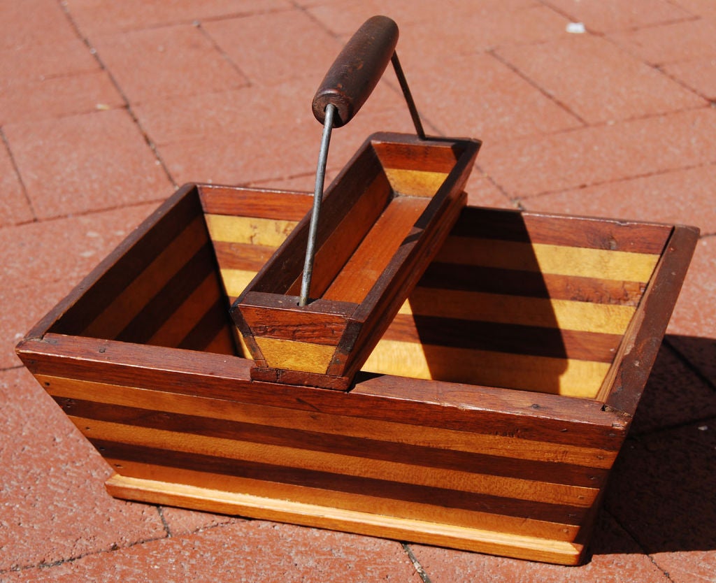 Sturdy basket decorated by stripes of cherry and maple wood. This graphic composition is continued through the tray on top. A turned handle is positioned at the top.