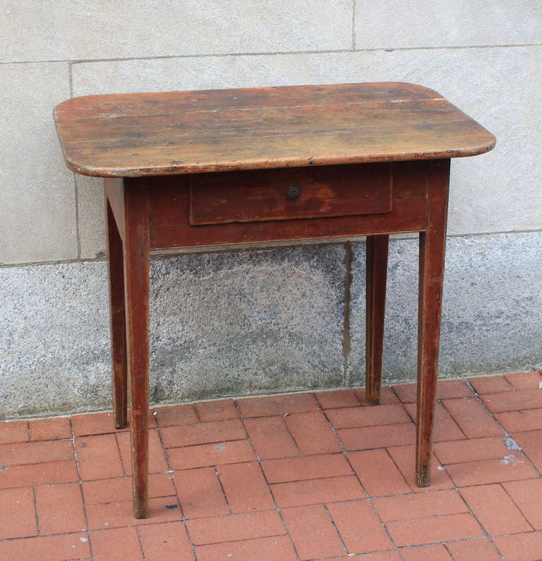 Pine server table with two-board top. The drawer is dovetailed and the face of the drawer over extends nicely on each side; the knob is replaced. Good tall height, rounded corners. Original red paint, scrub top, square tapered legs with carved
