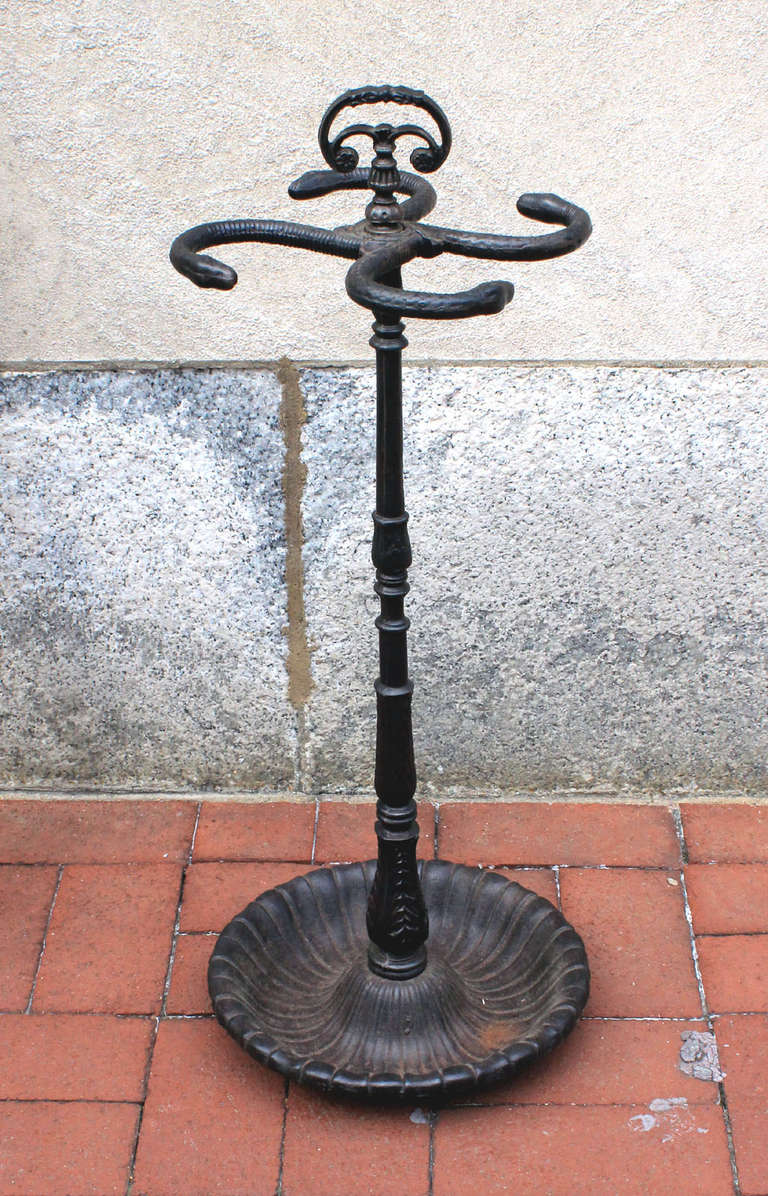 Heavy, cast iron Victorian umbrella stand with curving snake heads and leafy decoration at the base and up the shaft, and with a handle on top, circa 1870. Could perhaps be used for fireplace tools, as well.