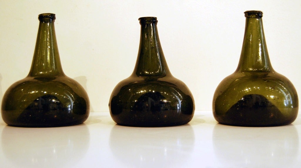 A fine little grouping of 3 dark green hand-blown glass onion bottles (so named for their shape). Their squat, sturdy-bottomed form indicates that they were made for use in a tavern or on a ship. Holland or England, 2nd quarter 18th century. Priced