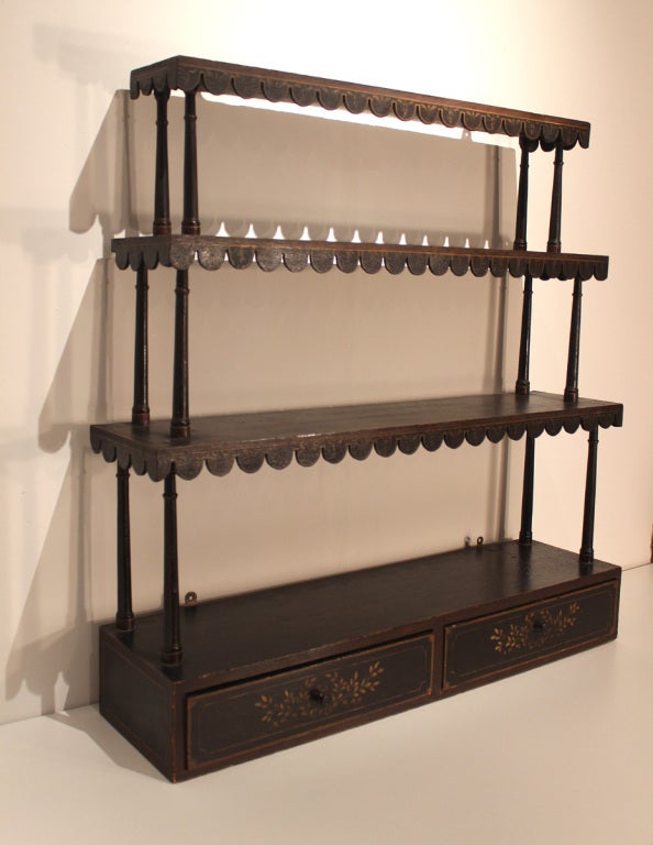 Handsome tiered hanging shelving unit with graduated shelves and two dovetailed drawers, wonderful scalloped apron to each shelf on three sides and nicely turned spindles; all in original excellent deep brown paint and gilt decoration, now with a
