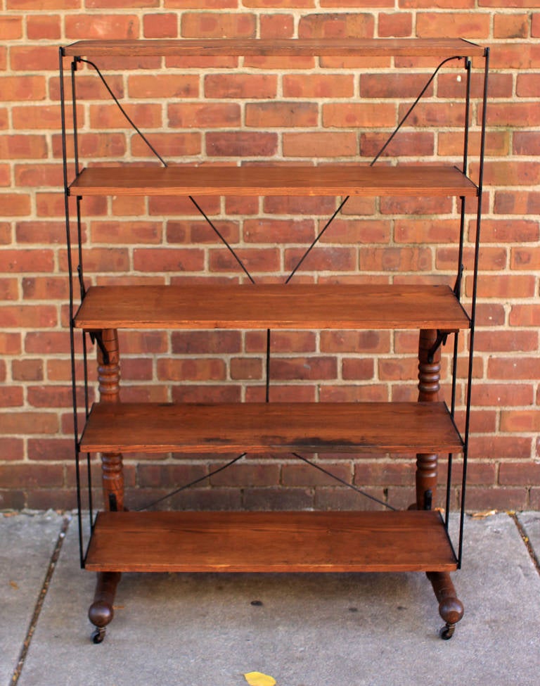 Highly interesting mechanical shelving unit that converts to a table surface. Iron frame with oak boards and turned legs/base, on casters. Has manufacturer's label - from Bryan, Ohio, circa 1900. All original. 

Note: The dimensions listed are for