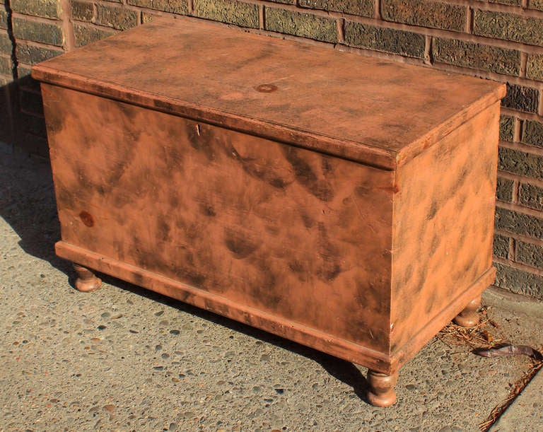 New England painted pine blanket chest with original smoke decoration over salmon paint. Very good size and with a till inside, with a secret drawer underneath. Dovetail construction and turned legs give the chest a nice little lift as well.