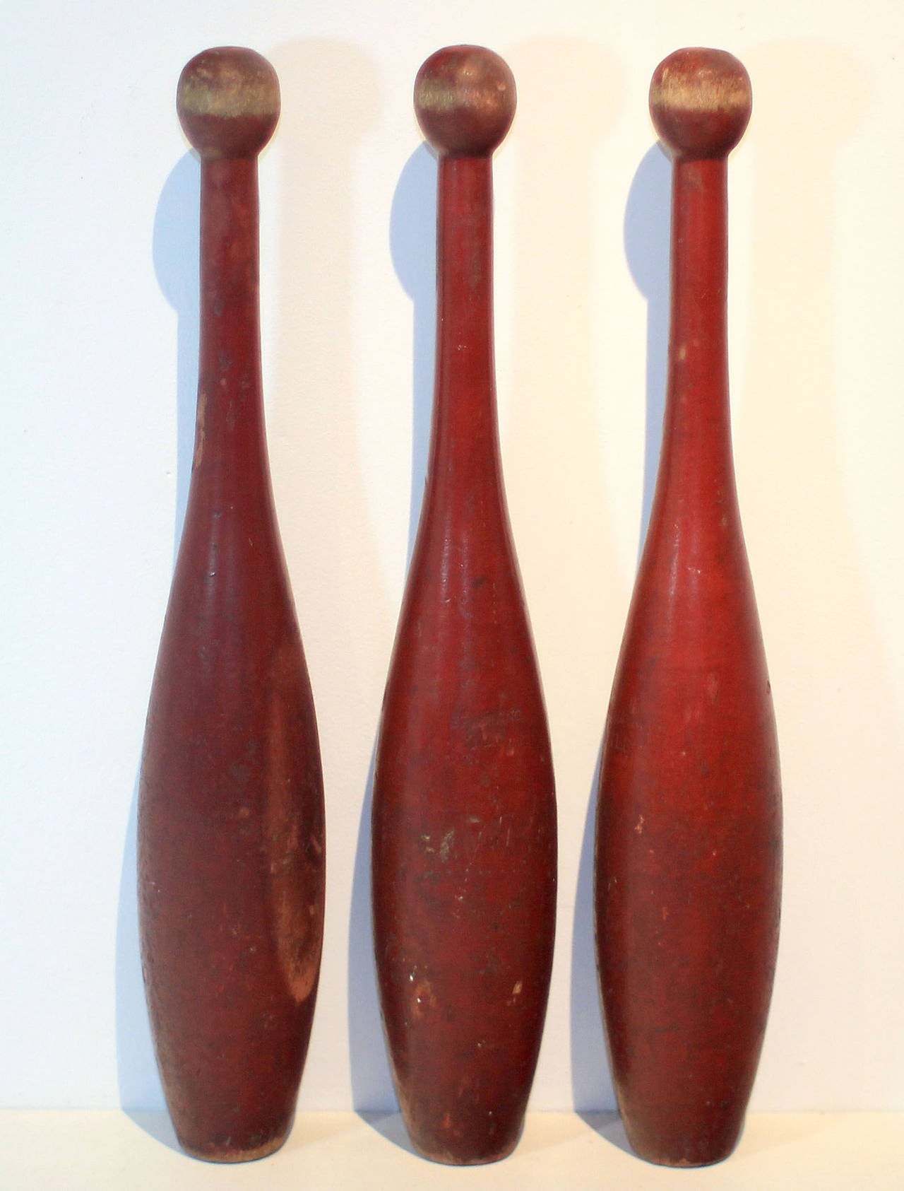 Set of three turned juggling pins in original red paint over wood, also were likely used as exercise pins. Graceful and with excellent color and wear. Each is stamped Spalding 1LB; early 20th century, American.