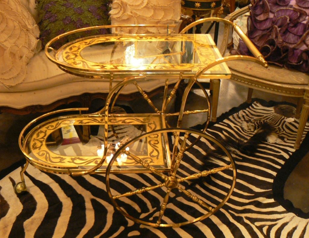 Beautiful tea or bar cart in classic Hollywood Recency design. Gold scroll design in both glass tops are in superb condition and no signs of wear or nicks to glass. Oversized wheels move well and very good maneuvering with the front caster.