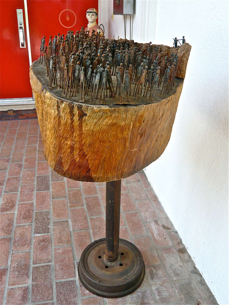A multitude of miniature metal human beings,some anatomically correct,welded together.They are mounted on a steel plate which in turn is fastened to a eucalyptus tree stump and set on a steel base.
