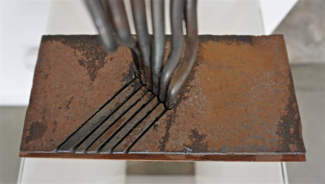 Six steel rods inserted on a steel base, twisted and flattened at the tips. The steel base has six diagonal cuts and is mounted on a wooden base.
Unsigned.