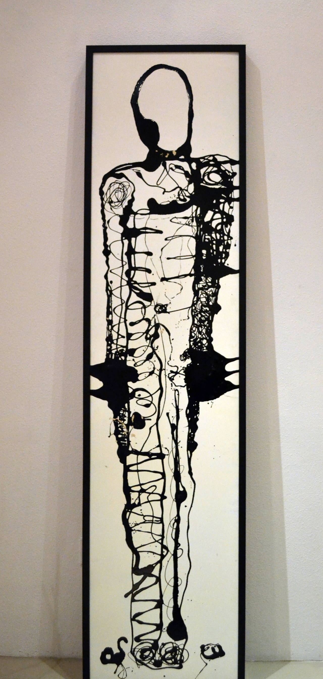 Standing 8 feet tall, this painting of a figure has been painted on plywood and then framed in a simple black molding. The artist Christopher aka Christopher Shoemaker (b. 1968) is self-taught. He used a technique of dripping acrylic paint onto the