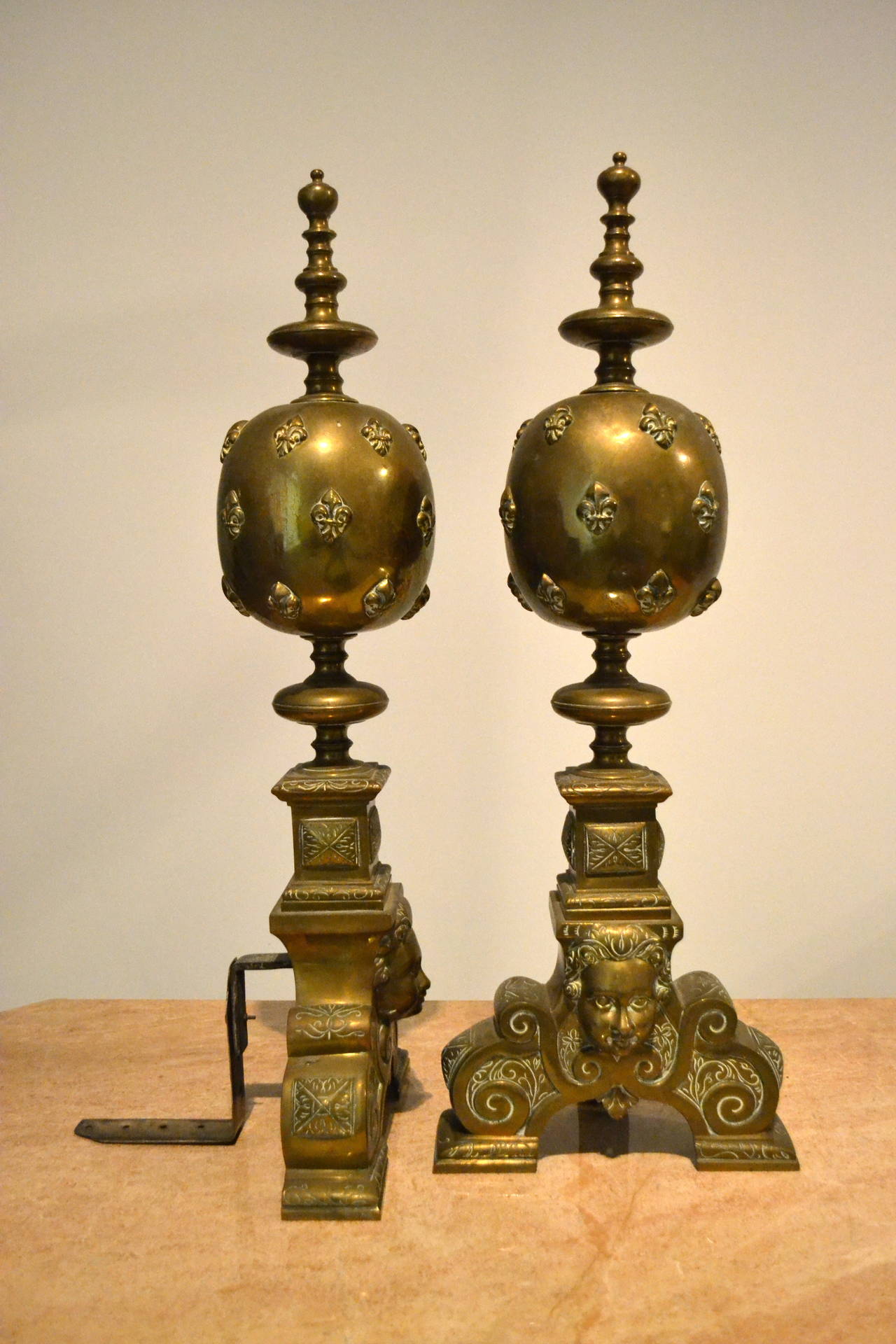 Pair of late 19th century to early 20th century impressive brass andirons with a fleur de lys motif and cherub faces at their bases.