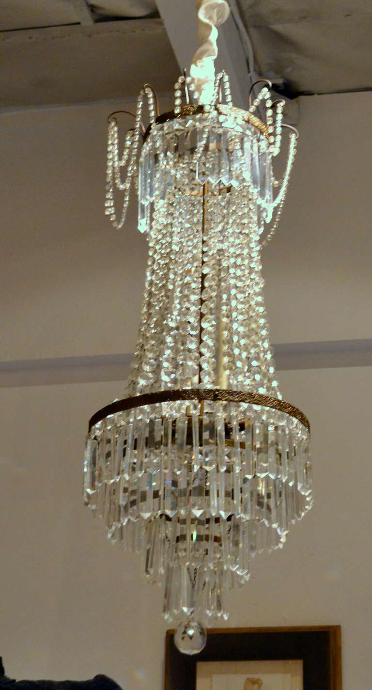 Draped in hand-cut crystals that help form the shape of this fine antique French Empire-style fixture. Created in the mid 19th-century or earlier, fitted with four interior candelabra bulbs that illuminate the entire fixture from the inside.