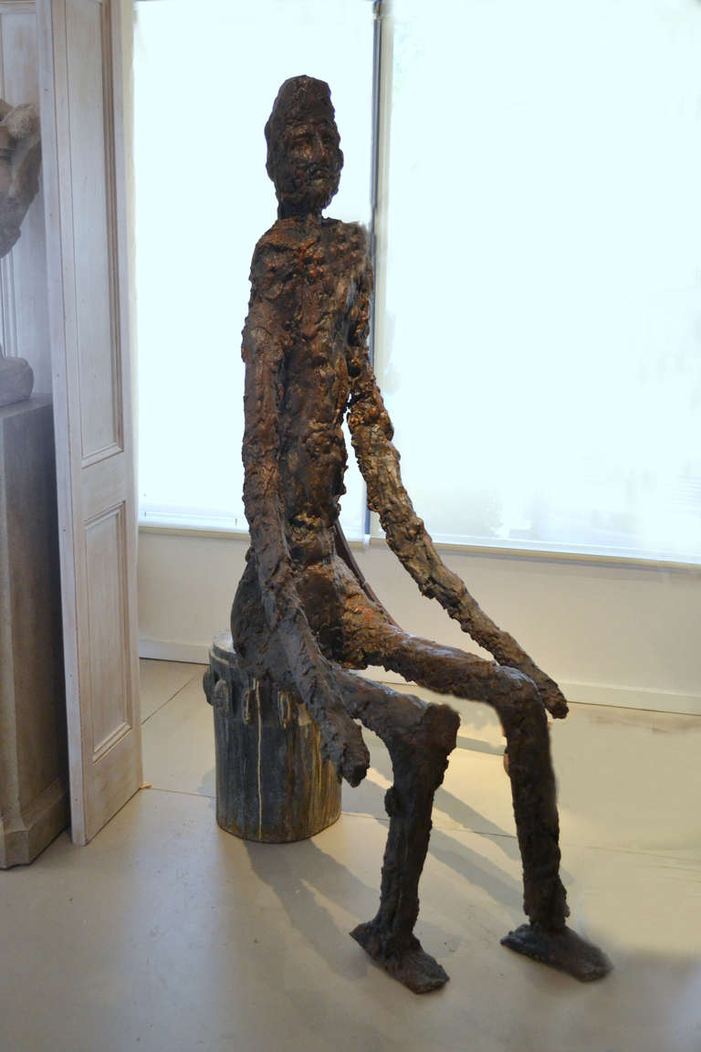 Artist Vladimir Prodanovich, (Yugoslavia, 1952) created this larger than life-size mixed media sculpture of a abstract figure in the Giacometti style, seated on a vintage wood carved plinth.  The sculpture is highly stylized with a textured