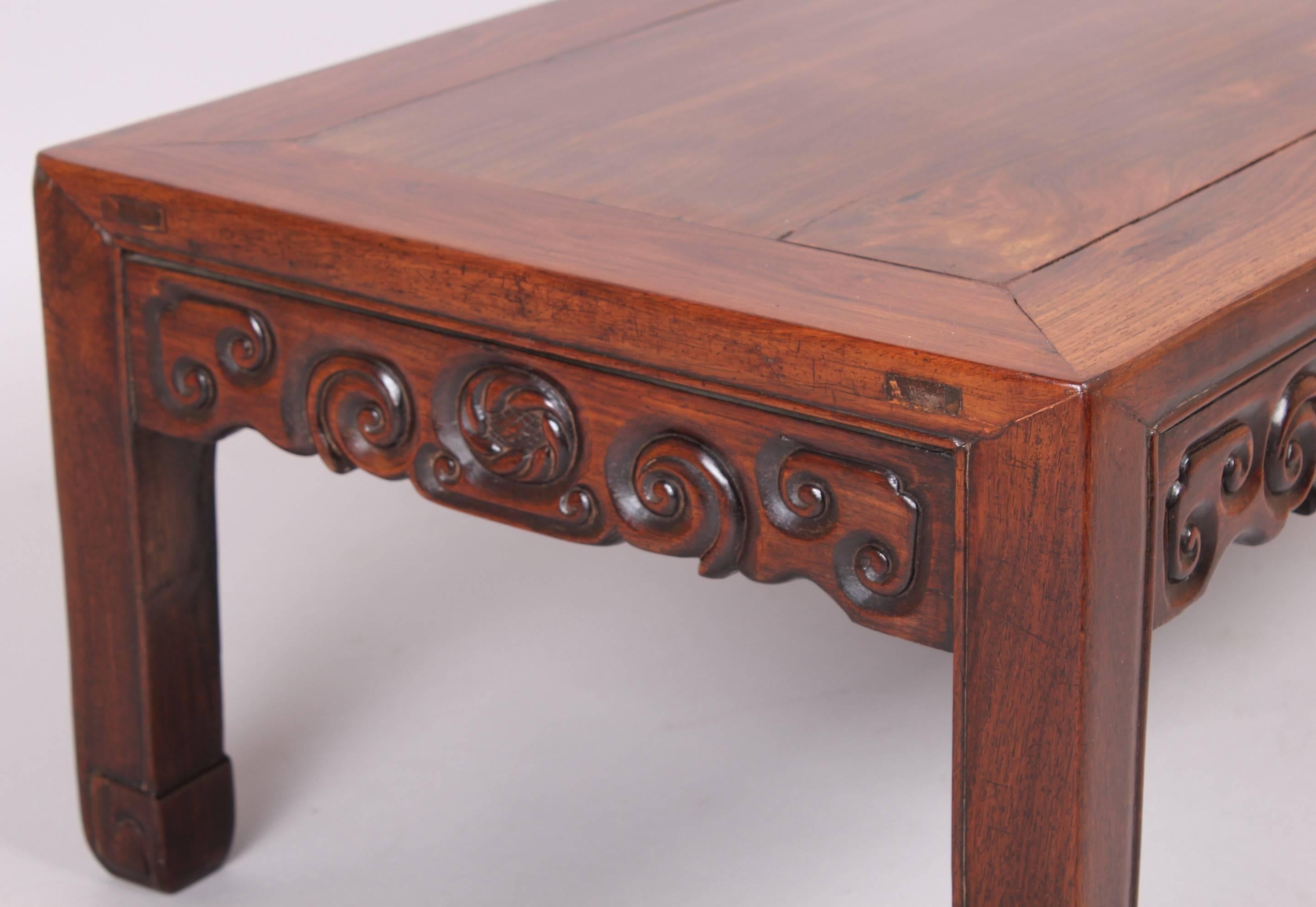 19th century Chinese hardwood, probably huanghuali, low tea-table; the cleated panel top mounted on a frame with carved traditional scrollwork motifs and on square legs.
 