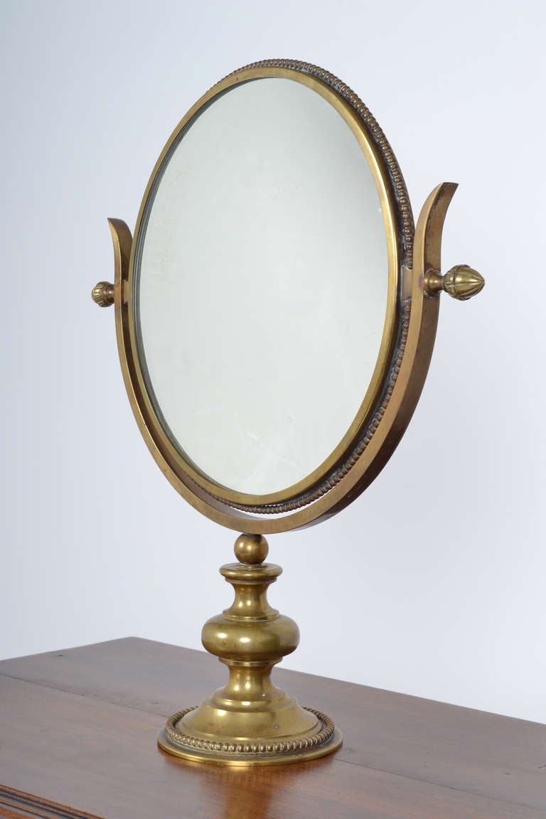 French antique double-sided table mirror, which rotates on a brass stand. Fine brass beading around mirror and on base, with acorn finials. A delicate and stylish piece.