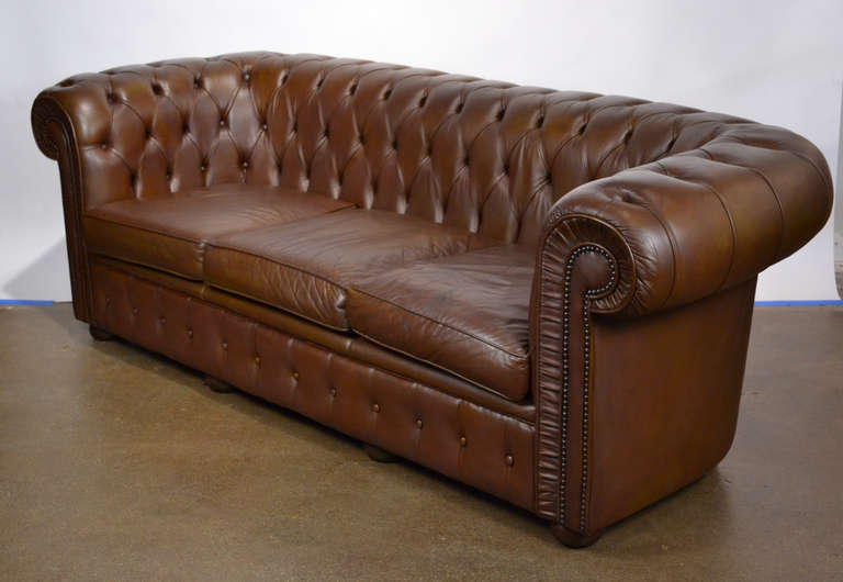 Vintage English Chesterfield leather sofa, with comfortable seats, beautifully tufted leather, and fabulous rolled arms and back. We love the modern proportions and wooden bun feet. Seat height is 18 in.