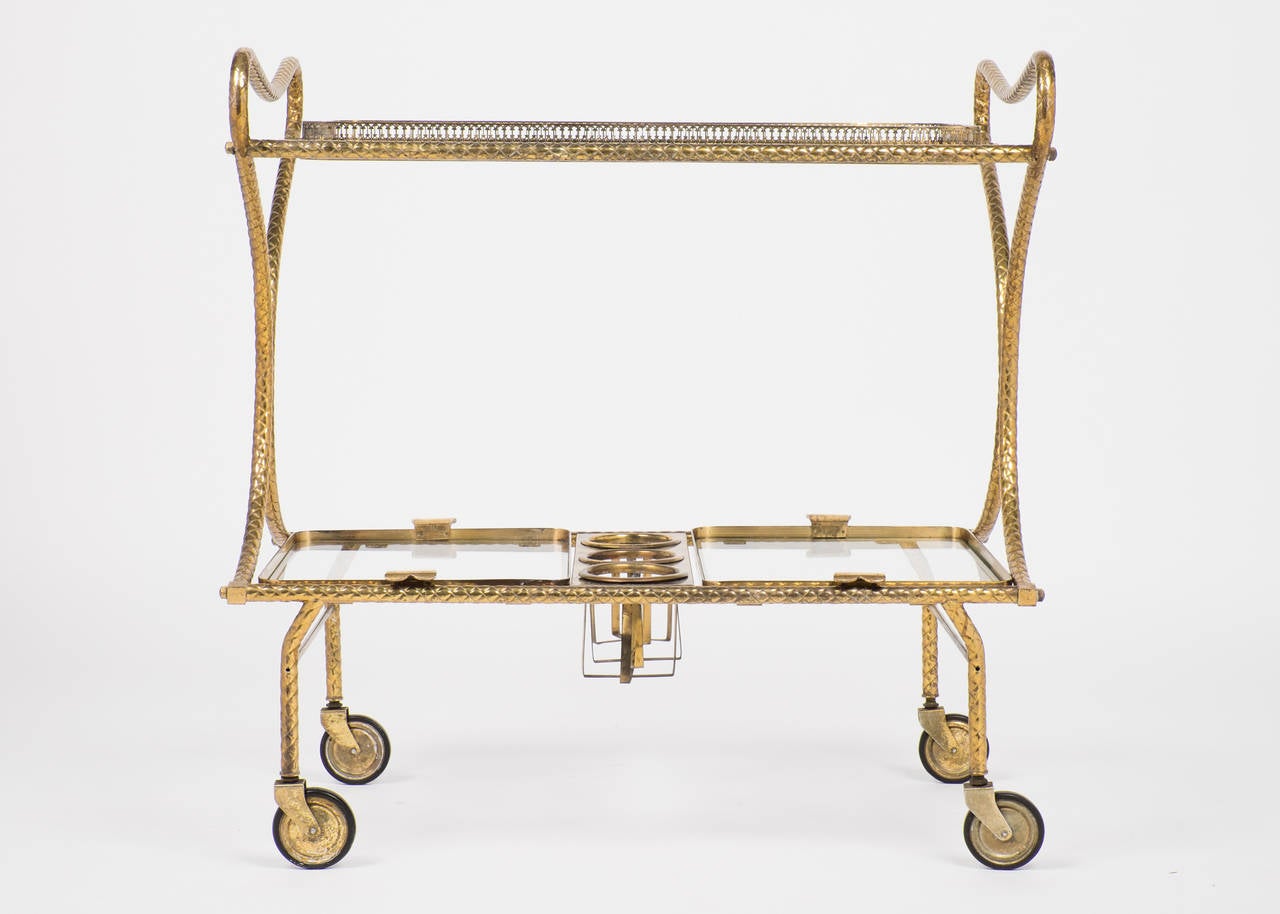 French vintage bar cart in brass with a rope design, two removable glass trays and three bottle holders. We love the unique style, with butterfly handles, the patina has kept its brilliance.