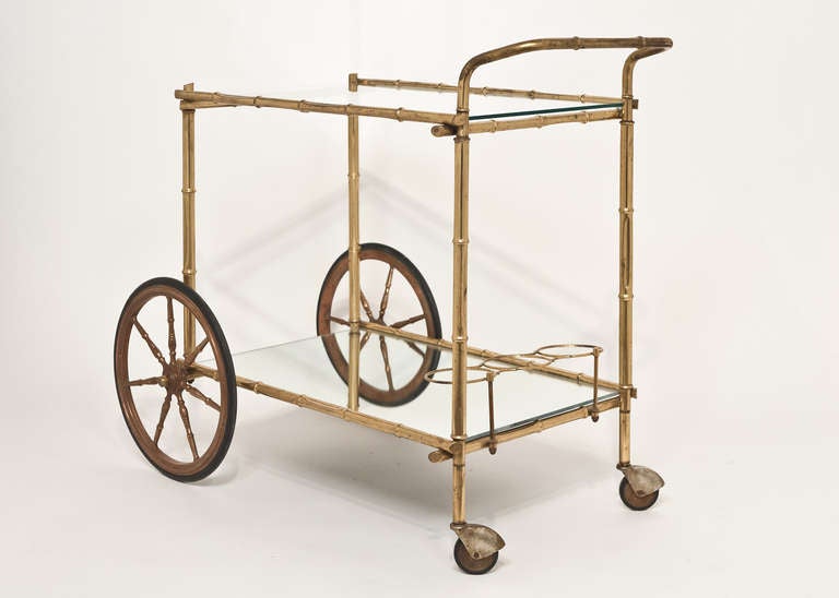 French vintage bar cart with bamboo style gilt brass frame, two glass shelves, and brass bottle holders. We love the large front wheels and great size on this stylish piece.