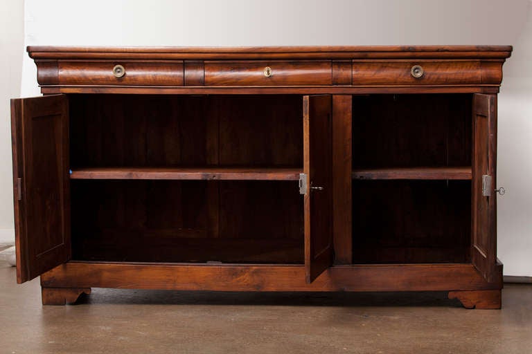 French Louis Philippe period enfilade  in solid walnut with three dovetailed drawers, three doors, and an interior shelf in each of two compartments. We love the scroll details on the feet and the characteristic 