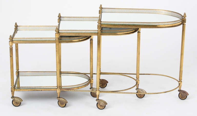 French antique set of three brass nesting tables on casters with acorn finials, finely cast galleries, fluted legs, and mirrored tops. The smallest table has a mirrored glass bottom shelf as well.