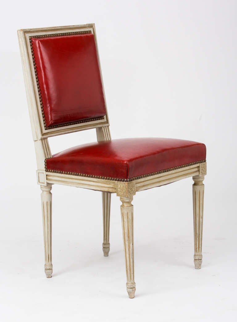 Set of eight French Louis XVI style dining chairs in hand painted beechwood with red leather upholstery and brass nail heads.