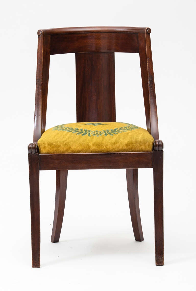 19th century French Empire style set of dining chairs in solid mahogany with original needlepoint upholstery. There are four different cross-stitched patterns - two of each on the eight chairs. I couldn't make myself replace the original needlepoint