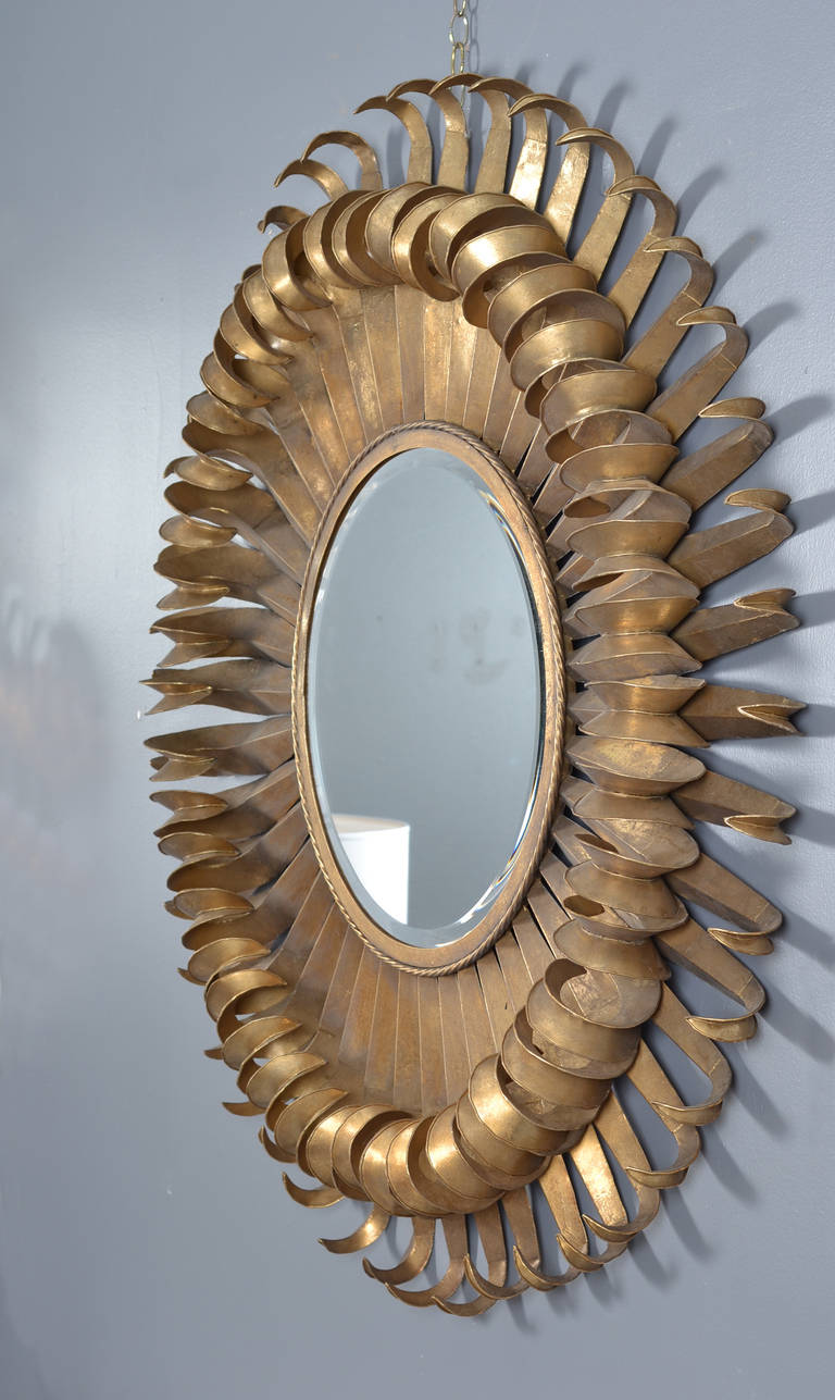 French  vintage sunburst mirror. Two overlapping rows of curling, gold leafed    rays surround the original, round, beveled glass mirror. In the manner of Line Vautrin.