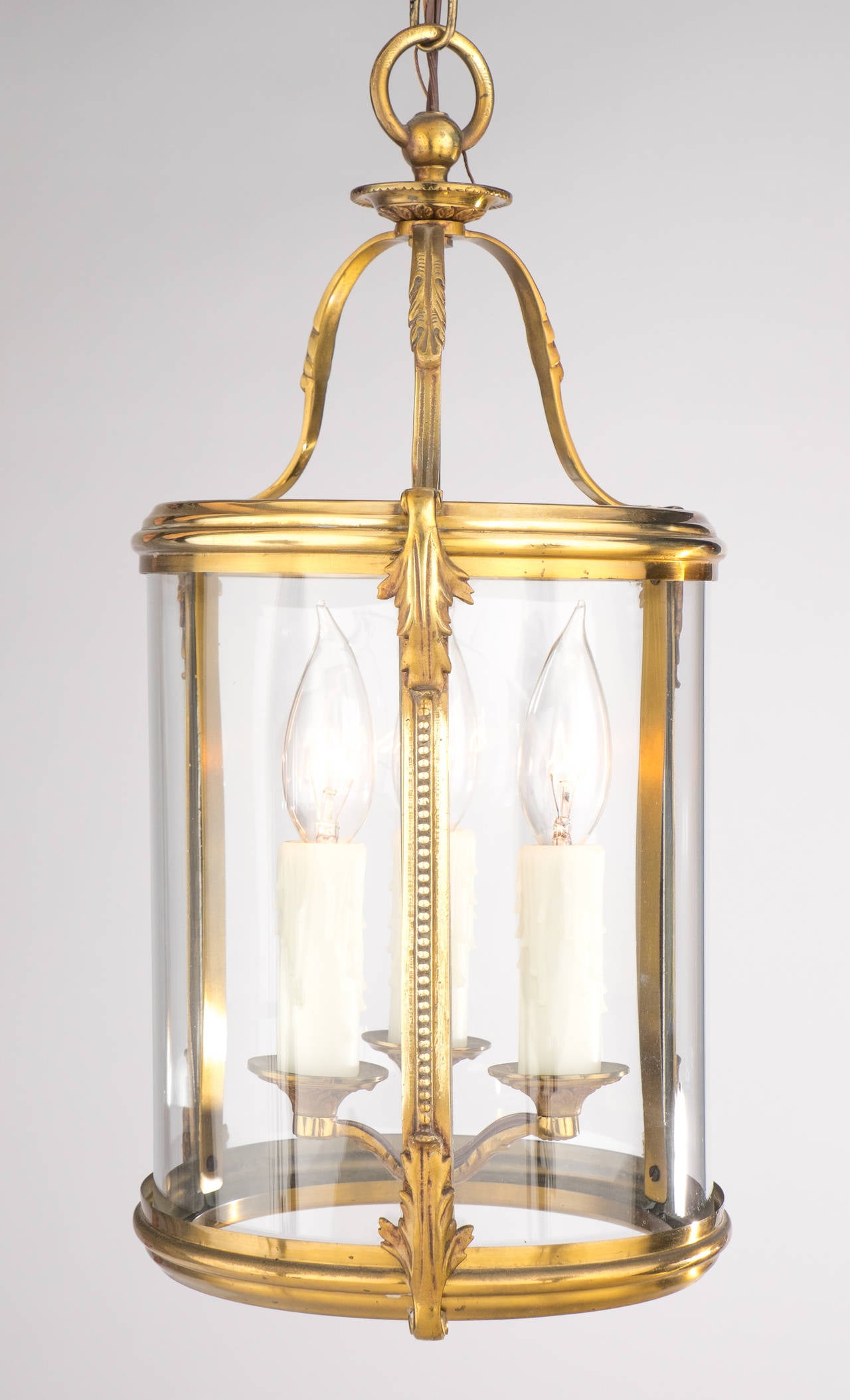 French 1920s pair of lanterns in finely cast brass and glass, with details of acanthus leaves and beading on the sides, each electrified with a three candelabrum cluster. Each fixture holds three candelabra base bulbs, rewired for the US. The height