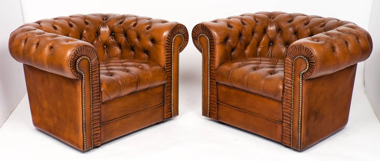 A comfortable pair of vintage English Chesterfield club chairs in a warm tan leather. Tufted seats and rolled arms, antiqued brass nailheads and wooden feet. All original in superb condition.