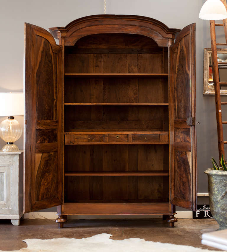 French Directoire armoire from the Rhone Valley, circa 1820, in solid walnut with figured walnut panels, fluted corners, and bonnet top. Peg construction. Interior contains four shelves with three dovetailed drawers, brass hardware. A majestic piece