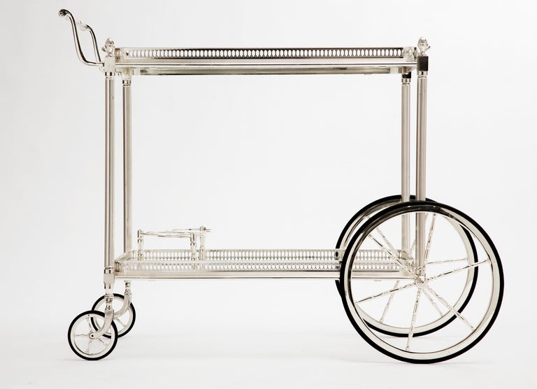 Vintage French bar cart in silver-plated brass with removable top tray, glass shelves, and bottle holder. We love the refined details in the delicate gallery, fluted legs, and acorn finials, as well as the stylized handle and large front wheels.