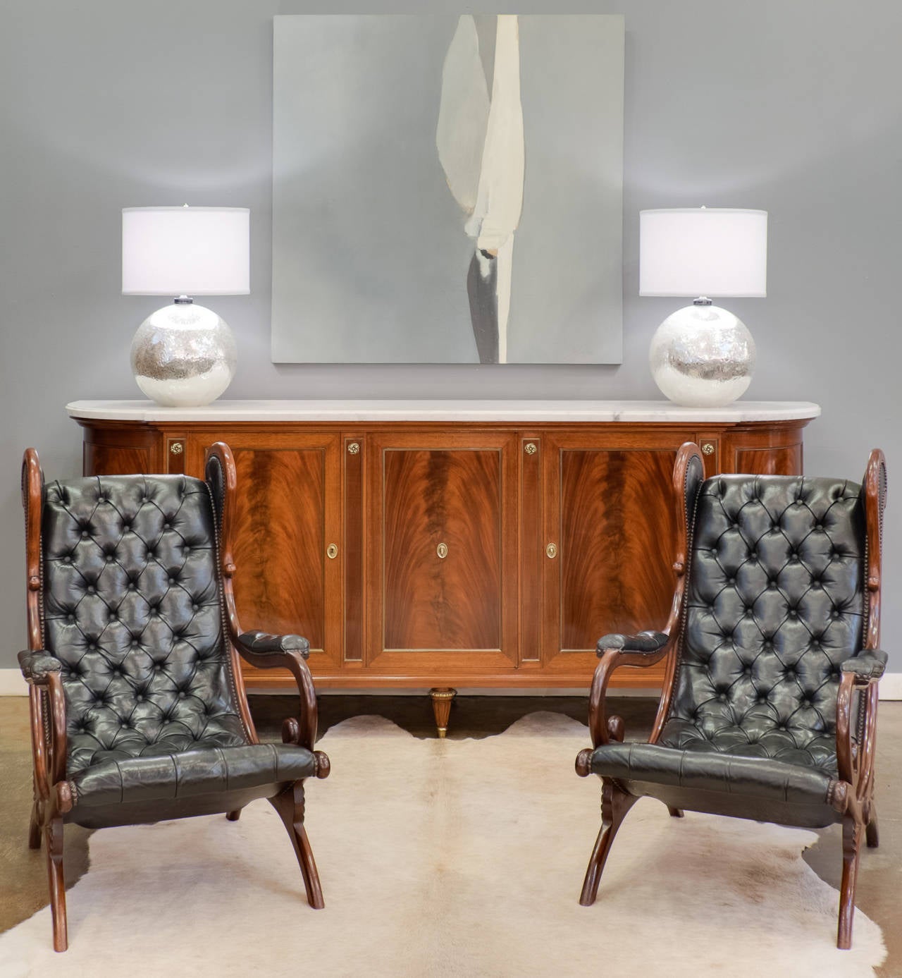 French vintage pair of lounge armchairs in carved mahogany with black leather upholstery. A personal favorite, these handsome armchairs are both comfortable and great looking! We love the curves, the carved details on the legs, and the tufted