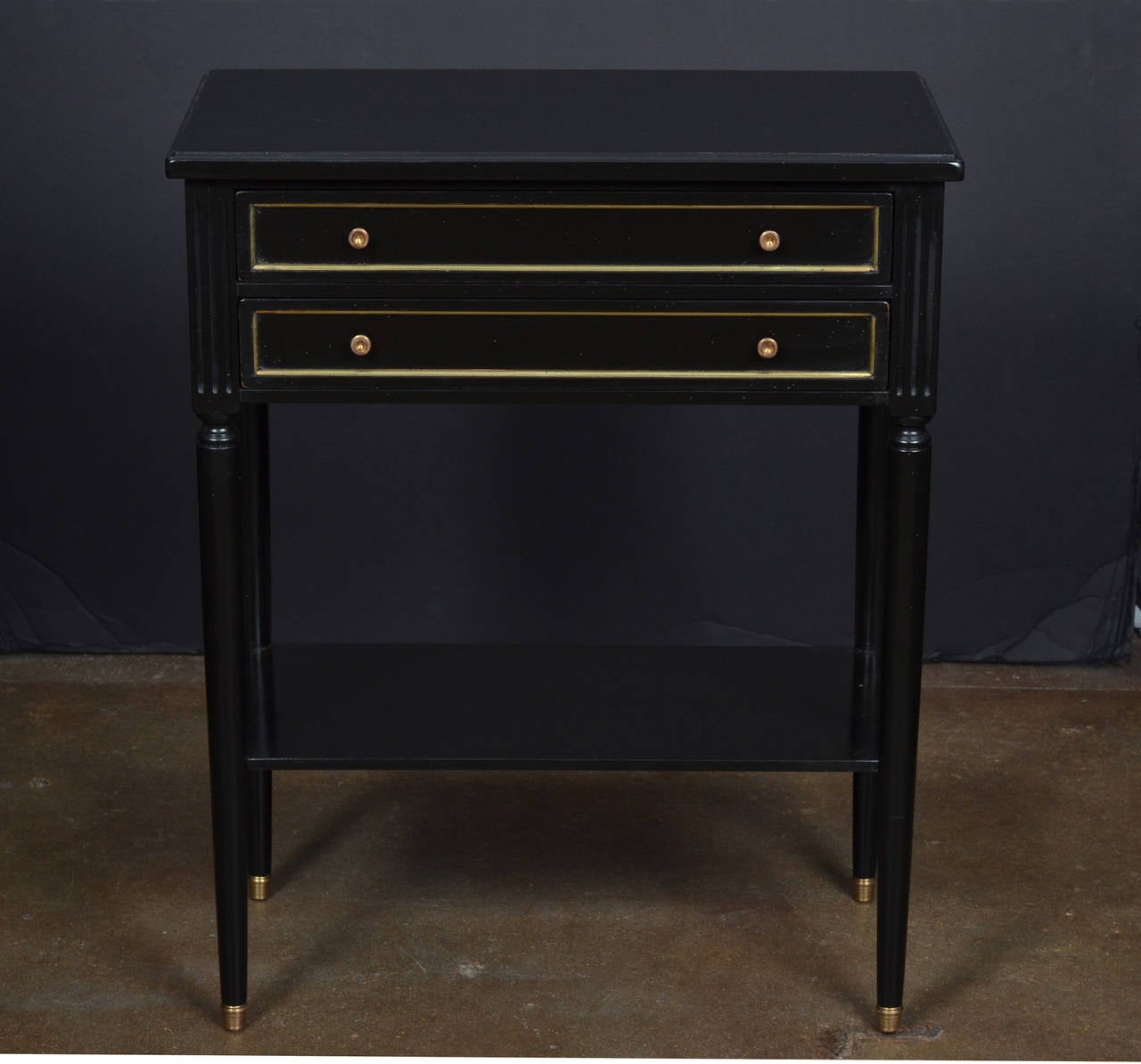 French Louis XVI style side or console table in ebonized walnut finished with a lustrous French polish. Two dovetailed drawers with brass trim and pulls, a bottom shelf, and brass capped feet.