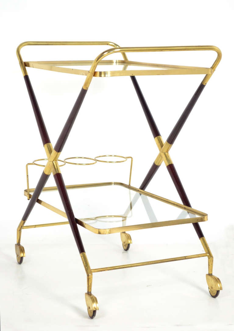 Italian vintage bar cart in brass and mahogany with two glass shelves, by Cesare Lacca. We love the sleek X profile, which also provides a handle on both sides of the cart, and brass bottle holder on the lower level. Mahogany legs are finished with