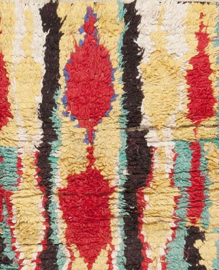 This charming Moroccan rug features a bold variety of elliptical medallions and ovular motifs surrounded by a rich variety of contrasting colors. The bold color palette includes bold cinnabar red medallions paired with white, Kohl black, turquoise