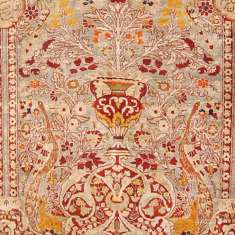 This magnificent antique Tabriz silk prayer rug almost has the effect pale gold jewels set with rubies. The field consists of a columned niche or mihrab enclosing a tree of life emerging from a vase. Peacocks stand at the summit of the tree and to