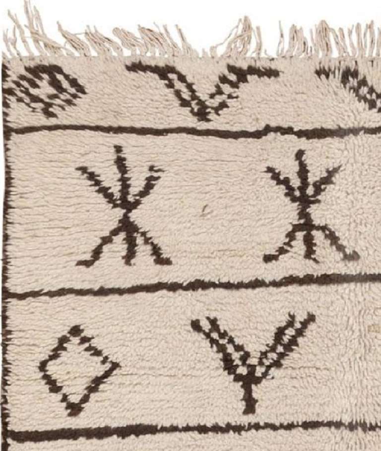Rendered in a clear, well-defined style, this bold vintage rug created in Morocco during the mid-20th century features a fantastic array of ancient symbols that are set over a sumptuous ivory-colored field. This timeless Moroccan rug showcases a
