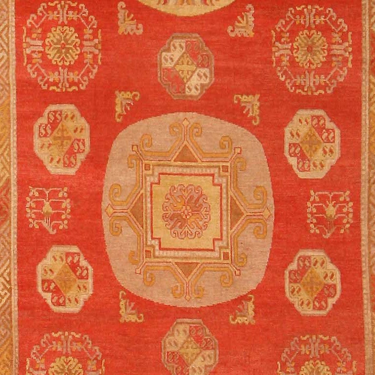 Antique Khotan, East Turkestan, late 19th century a Classic East Turkestan design of large and small golden medallions floats amidst a warm red field on this stately antique Khotan. The larger scale and solid form of the central medallions are