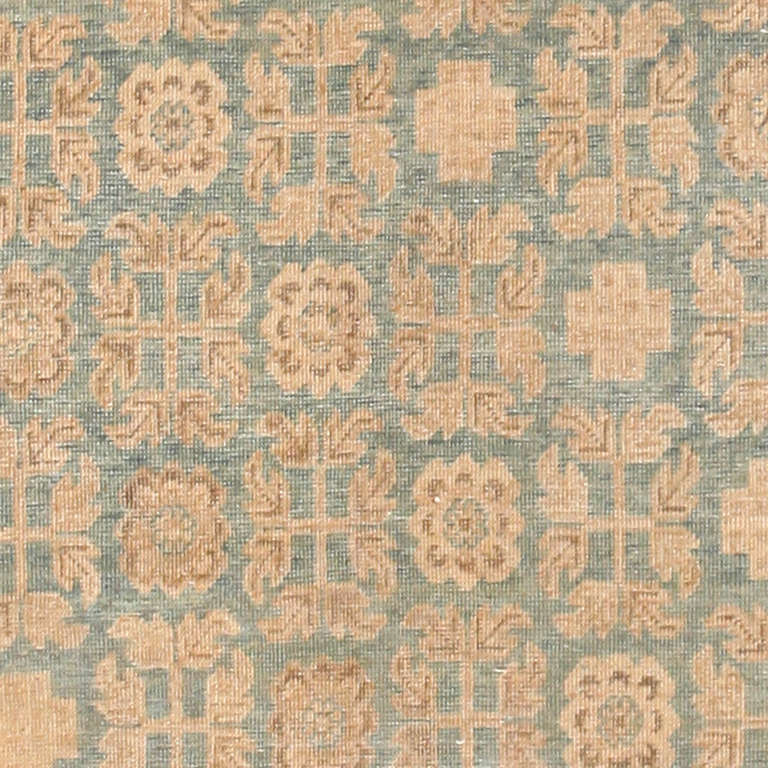  Crafted along a cultural crossroads on the cusp of the Far East, this antique Khotan carpet reflects a diverse set of international design traditions. The stately verdigris field is dotted with ornamental rosettes and alternating quatrefoils that