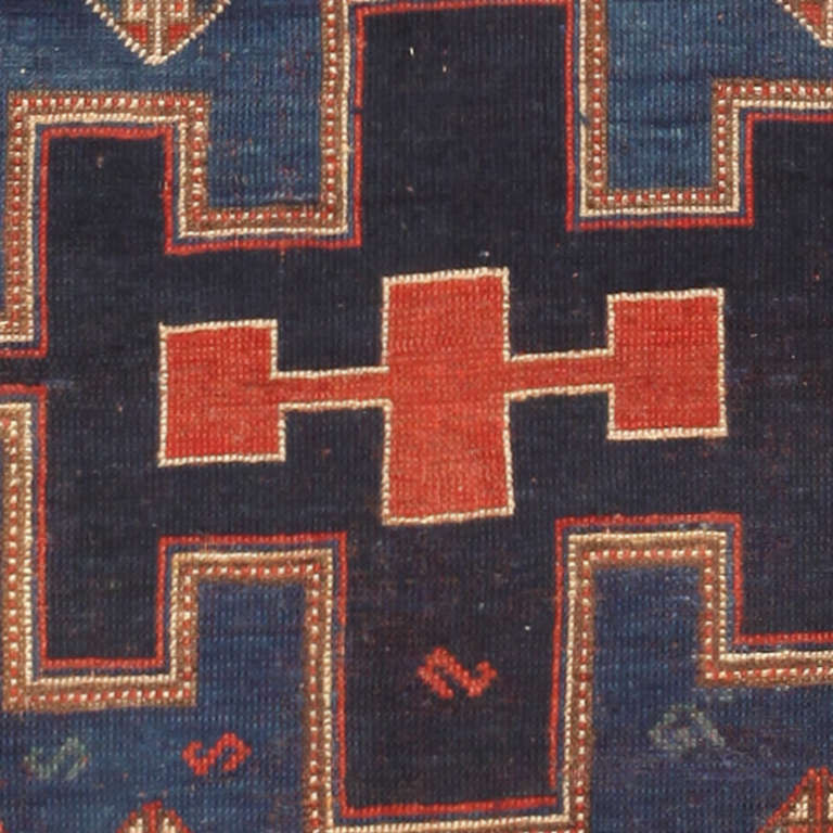 This dazzling antique Caucasian Kazak carpet showcases a marvelous triple medallion that displays searing lines, strong colors and clear rectilinear decorations rendered in a stunning pairing of jewel-tone blue-greens and fiery vermillion reds. The