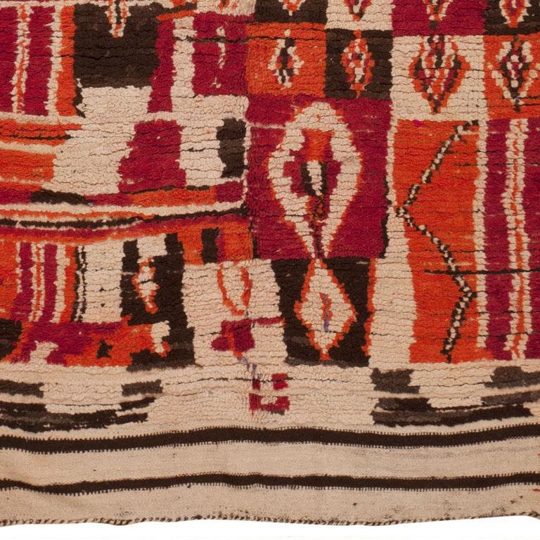 Created in Morocco circa 1940, this expressive vintage rug features graphic geometric patterns decorated with auspicious symbols that are rendered in a bold combination of cerise, Vermillion and walnut brown set over an oatmeal-colored field.