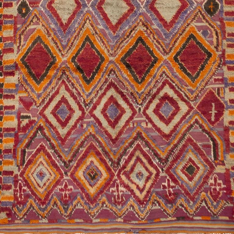 This outstanding vintage Moroccan rug depicts a splendid repeating pattern with bold polychromatic lozenges, luxurious plush pile and complex zigzagging outlines. The bold color scheme features warm orange hues, strong mulberry reds and cool
