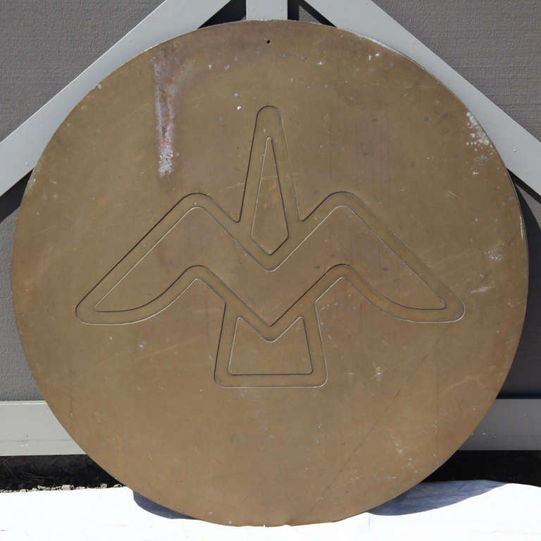 Round bronze sculptural disk featuring the emblem of a bird with outstretched wings. 