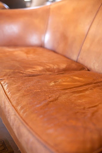 Leather Settee with original tanned leather distressed into wonderful dark tobacco color. Nail head trim and square wooden feet.