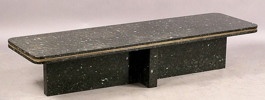Long Mid-Century modern, brass trimmed black granite coffee table. Top has rounded corners and rests on cruciform base.