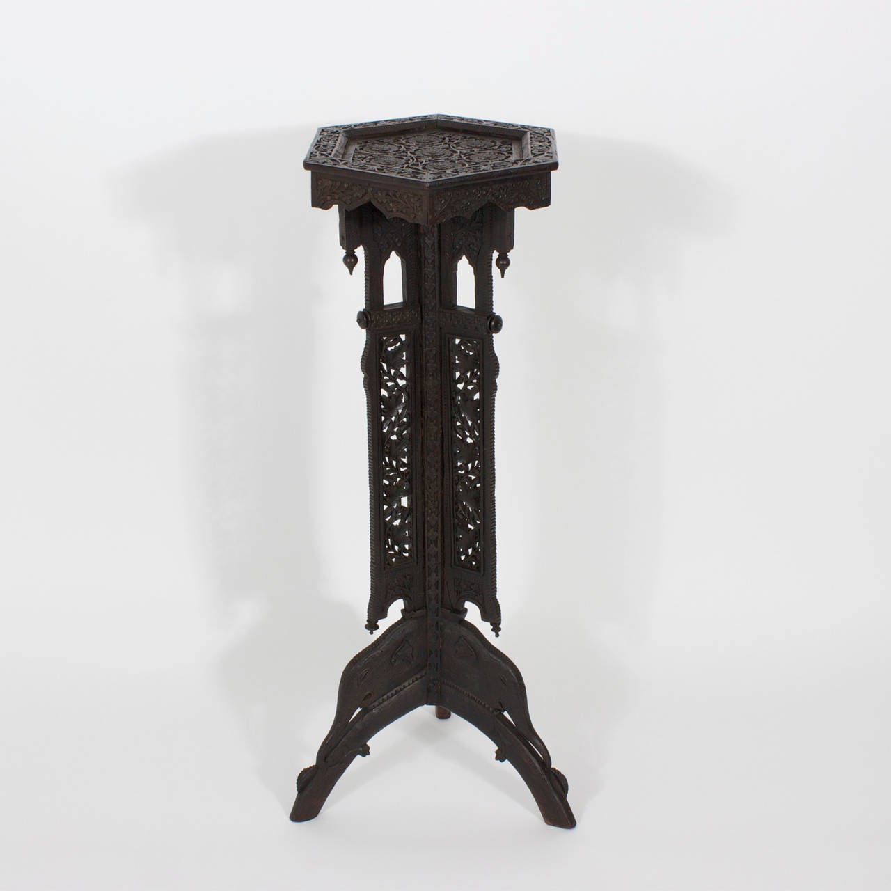 Intriguing, finely carved, hardwood Anglo Indian pedestal with a hexagonal top and scalloped skirt over an architectural trunk with finials and 3 floral carved panels terminating in stylizied elephant head legs.