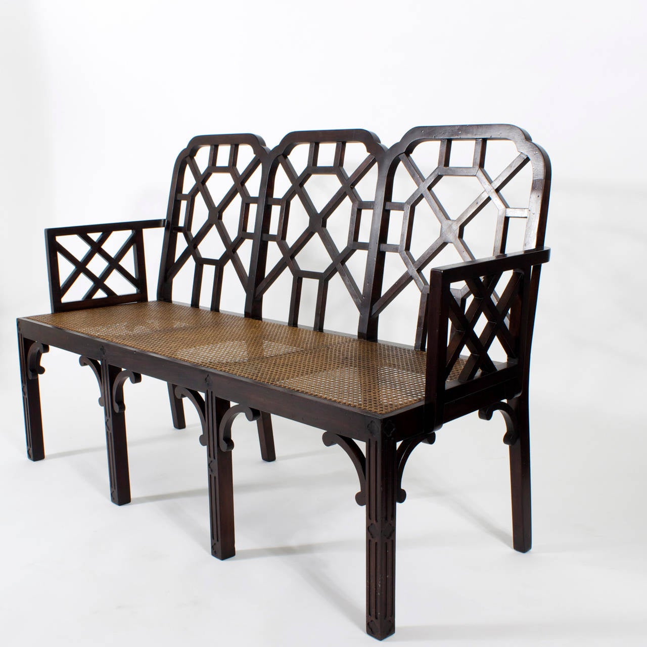 A mid century Chinese Chippendale settee with a polished ebonized finish, caned seat, open fret work lattice or trellis back and arms, with straight paneled  legs and stylized bracket supports. An over all modern take on a timeless form. Newly