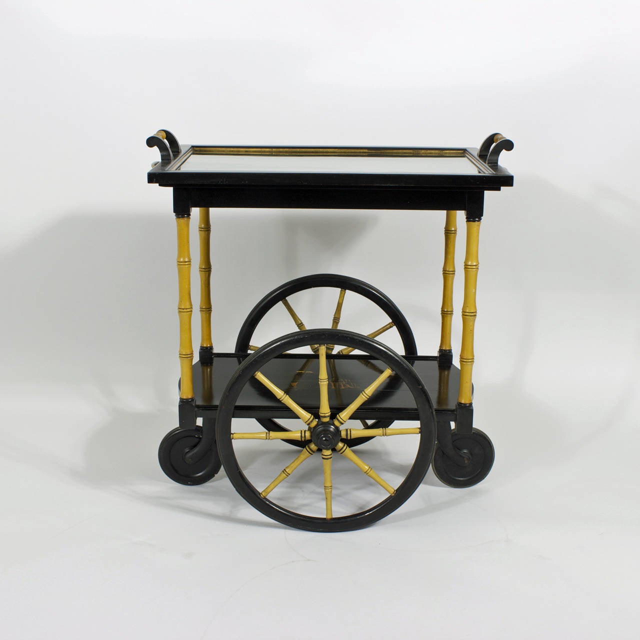 A mid century, tea or bar cart sometimes known as a drinks trolley executed in a light hearted chinoiserie style, lacquered in black with faux bamboo posts and spokes, a great play of tan and black color combinations.  Decorated in a classic Chinese