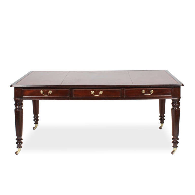 A George III library table or partners desk, 6 working drawers, 3 on each side, with a red tooled leather top, turned and reeded legs, panelled ends, cup casters and molded drawers. Original hardware.  All and all, a beautiful piece of furniture.